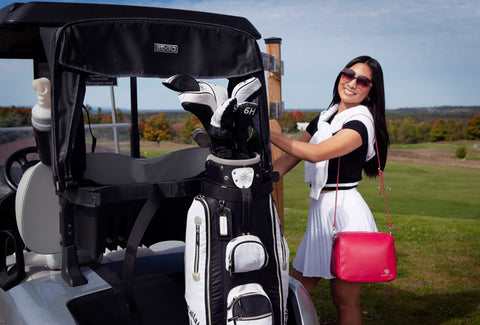 Image of a woman wearing a La Coutts Toronto Thermal Handbag in front of a Golf Cart at a golf course