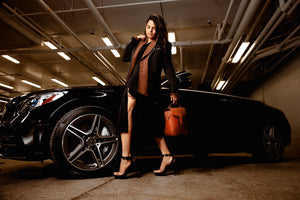 Image of a girl standing in front of a black Mercedes. The girl is holding a brown Duncan thermal designer handbag by La Coutts Toronto